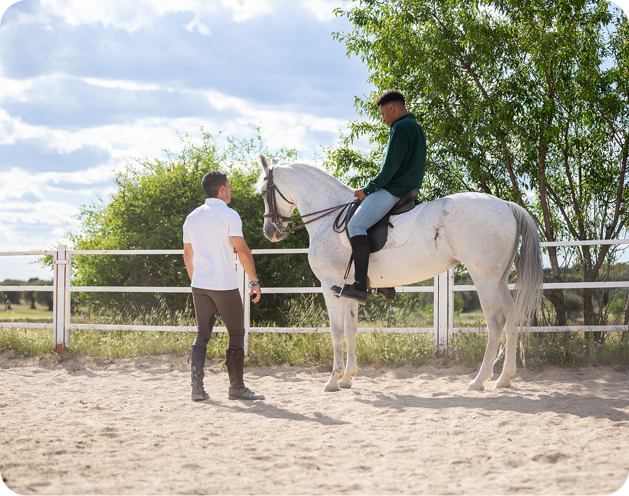 Horseback rider with trainer in sunny arena.