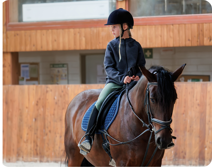 Kid in helmet horseback riding indoors
