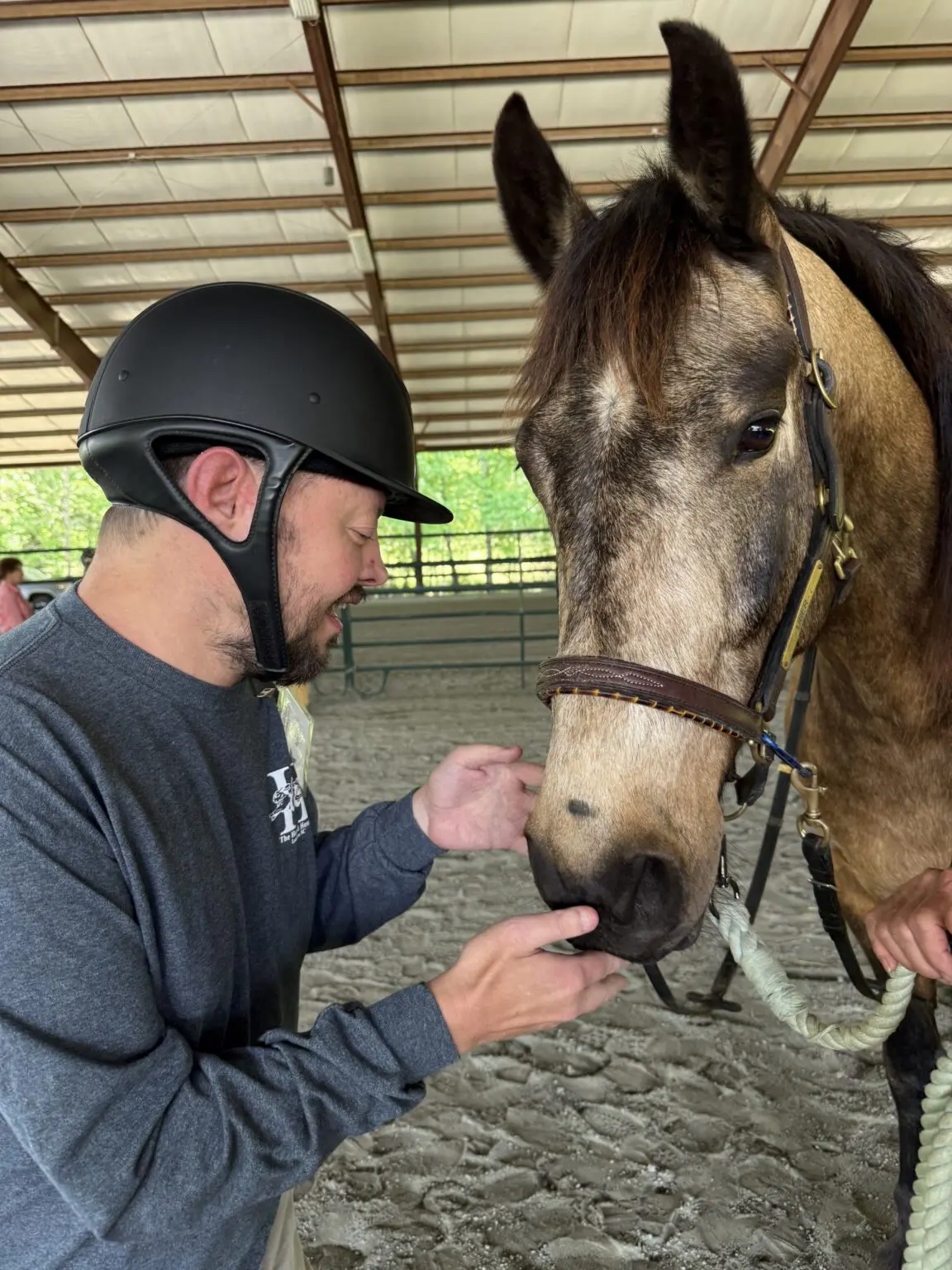 Man in helmet feeding horse in arena
