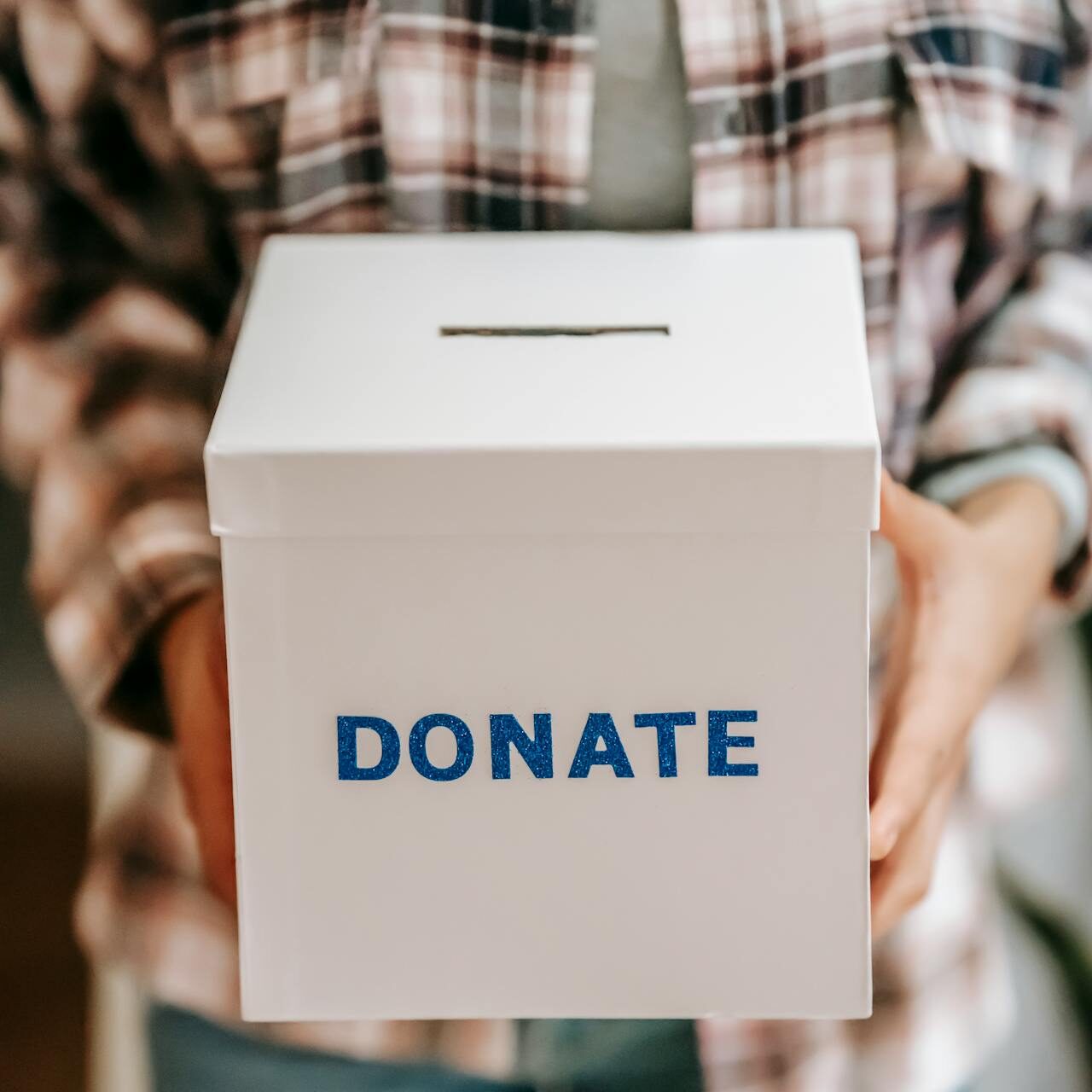 Person holding white donation box labeled DONATE